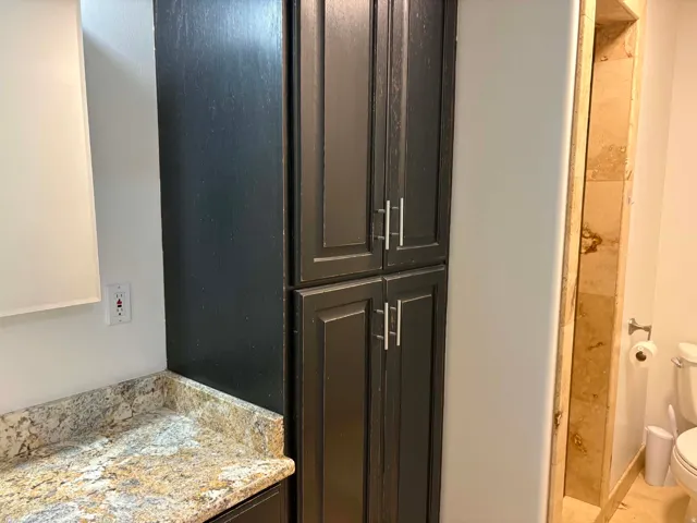 Granite countertop, dark wood-finish cabinetry with silver-tone hardware, and tiled wall accents