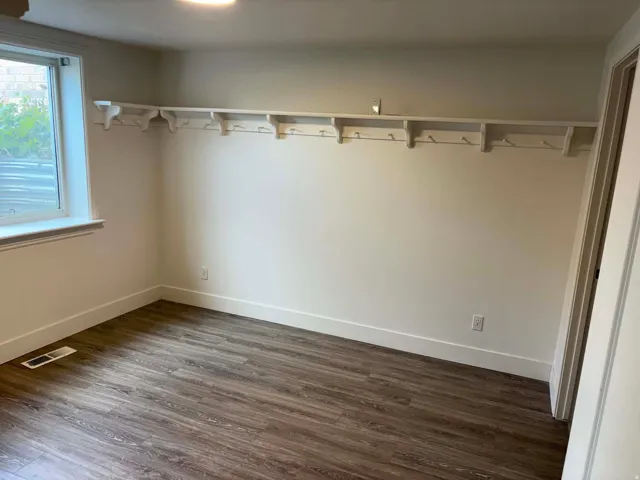 Wood-finish flooring with white baseboards and trim, featuring a built-in wall shelf with coat hooks, and an attached ceiling light fixture
