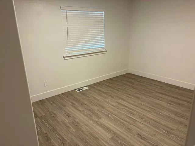 Wood-finish flooring with white baseboards, a window featuring horizontal blinds, and neutral wall tones