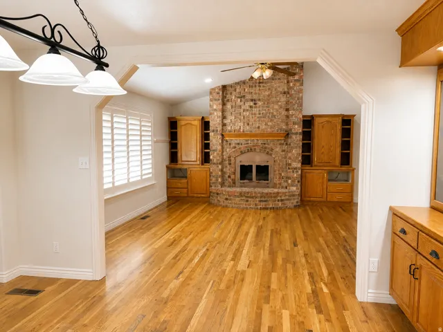 Hardwood flooring throughout, a brick-surround fireplace with a wood mantel, built-in cabinetry, and white plantation shutters