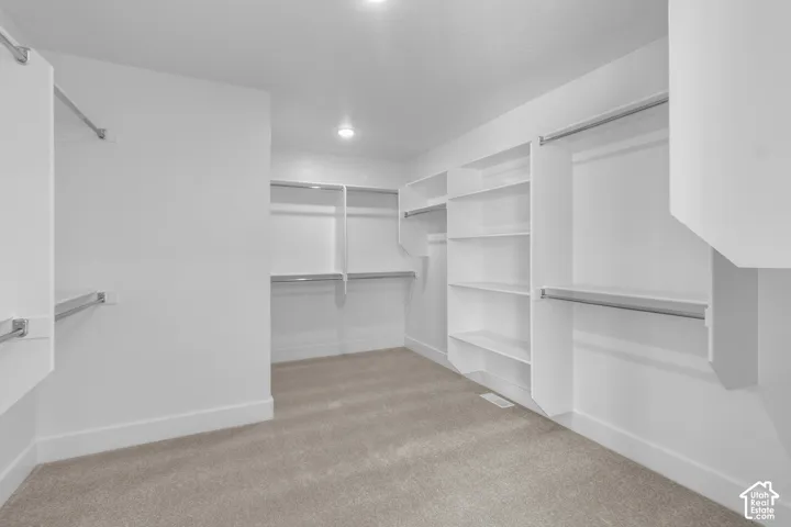 Spacious closet featuring built-in white shelving, chrome hanging rods, recessed lighting, and carpet flooring