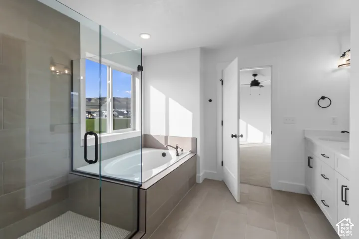 Glass-enclosed shower with subway tile surround, separate soaking tub, expansive window, and a vanity with an undermount sink