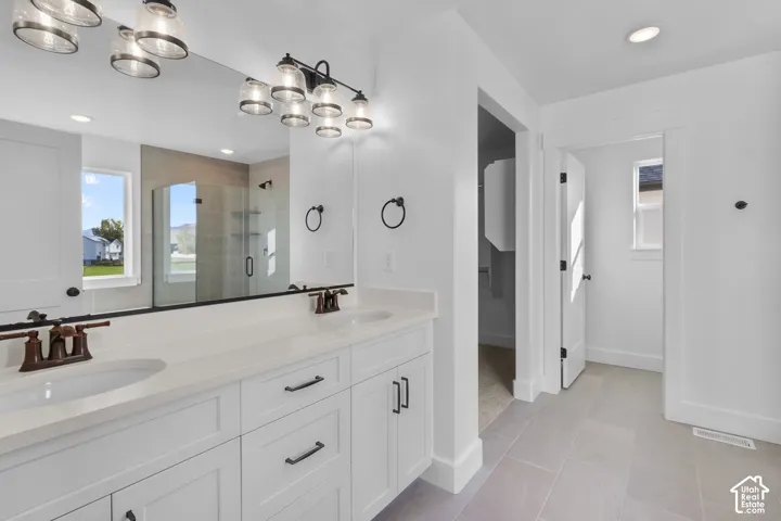 Dual vanity with white cabinetry, bronze-finish fixtures, and a glass-enclosed shower
