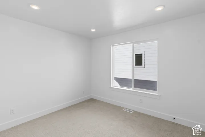 Recessed ceiling lighting, white painted walls, carpeted flooring, and a large sliding window