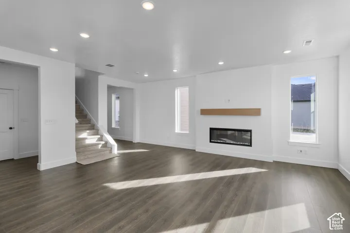 Spacious living area featuring wood-finish flooring, a contemporary linear electric fireplace with wood mantel, recessed lighting, and a carpeted staircase