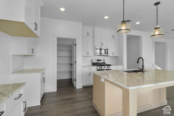 Kitchen featuring white cabinetry, stainless steel appliances, a center island with a sink, pendant lighting, and wood-finish flooring