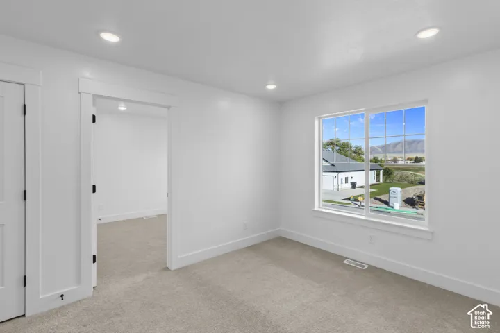 Recessed ceiling lighting illuminates a room with light-colored carpeting, white walls, and a large window featuring multi-pane grids