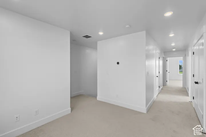 Recessed lighting, light neutral-toned carpeting, white walls, white doors with black hardware, and white trim
