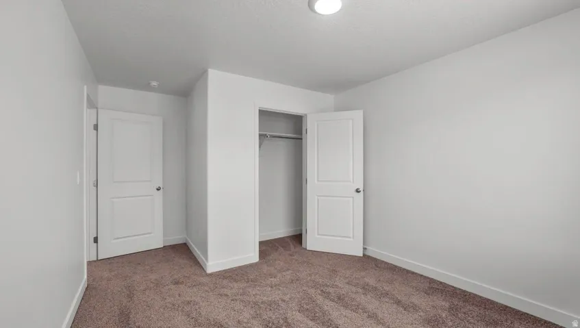 Bright interior with white walls, brown carpet flooring, recessed lighting, and a built-in closet with hanging rod