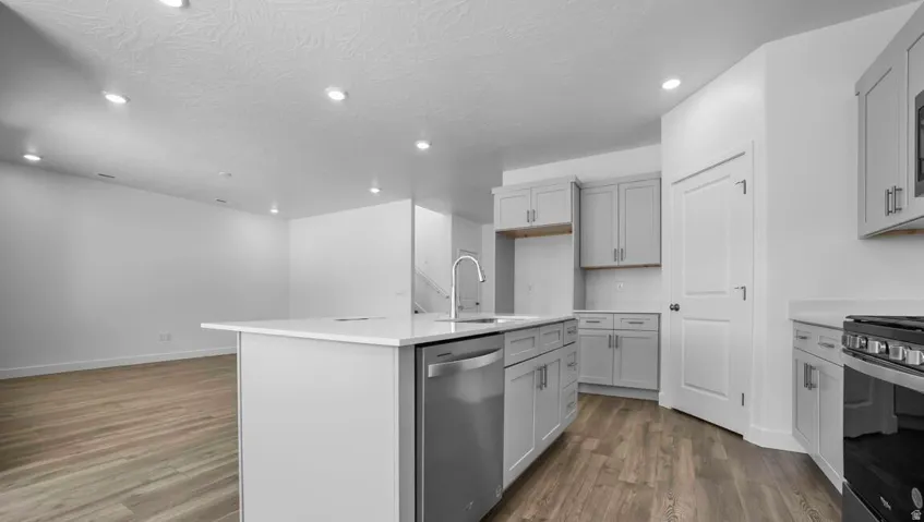 Modern kitchen featuring light gray cabinetry, stainless steel appliances, a center island with a sink, and light-toned countertops