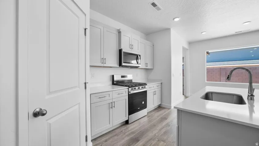 White shaker cabinetry with stainless steel appliances, wood-finish flooring, recessed lighting, and a kitchen island with an undermount sink