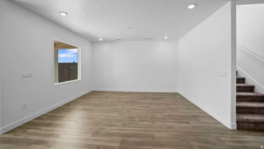 Spacious room featuring wood-finish flooring, recessed lighting, a large window, and broad baseboards