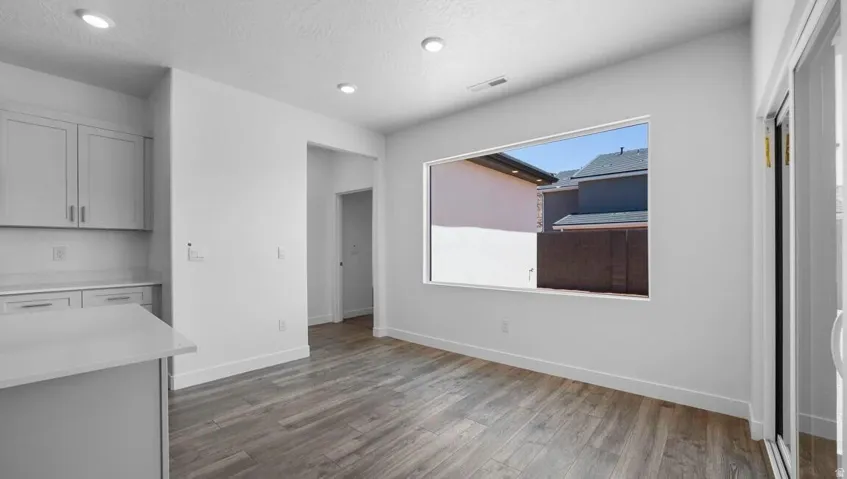 Recessed lighting, wood-finish flooring, white shaker-style cabinetry, white countertops, and a sliding glass door