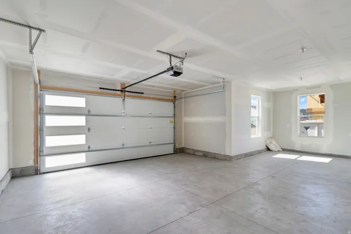Spacious garage with a sectional garage door featuring frosted panels, two windows, and exposed ceiling joists