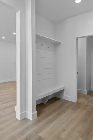 Built-in bench with coat hooks, wood-finish flooring, recessed lighting, and white trim