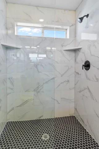Walk-in shower featuring a glass enclosure, white marble-look wall tiles, and black hexagon floor tiles