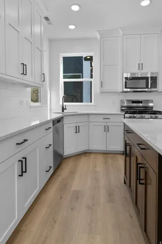 White shaker-style cabinetry, matte black hardware, stainless steel appliances, wood-finish flooring, and a white subway tile backsplash