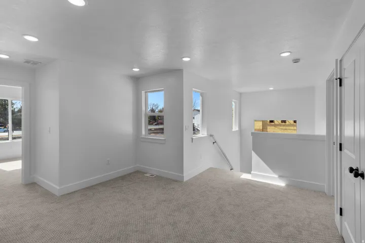 Loft space featuring recessed lighting, light-colored carpeting, multiple windows, and a half-wall partition
