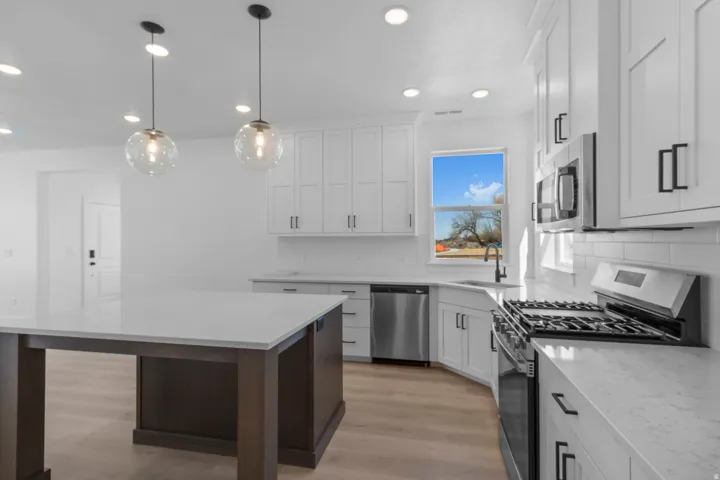 Kitchen featuring white shaker cabinetry, stainless steel appliances, a center island with a light-toned countertop, wood-finish flooring, and pendant lighting