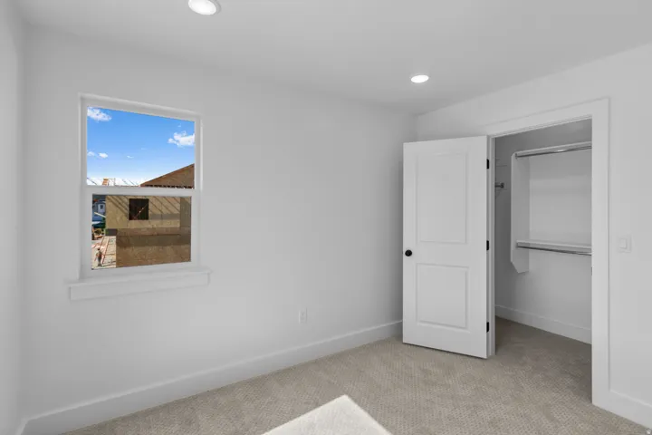 Recessed lighting, wall-to-wall carpeting, window with white trim, and a paneled door leading to a closet with built-in shelving and hanging rods