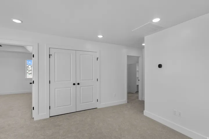 Recessed ceiling lighting, paneled bifold doors with matte black hardware, and light-toned carpeting