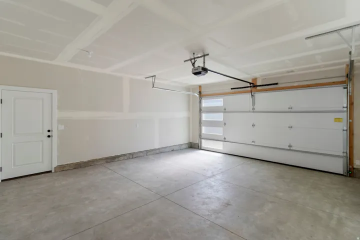 Spacious garage featuring a concrete floor, overhead lighting, an automatic garage door opener, and a panel door with black hardware