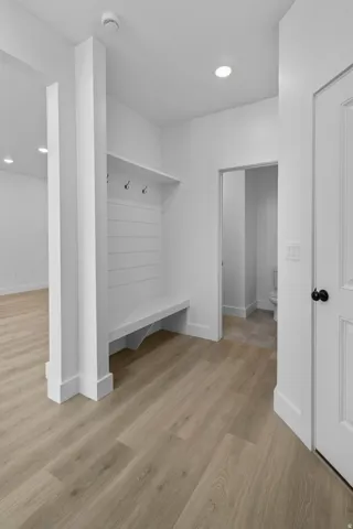 Built-in mudroom bench with coat hooks, wood-finish flooring, recessed lighting, and white paneled door with matte black hardware
