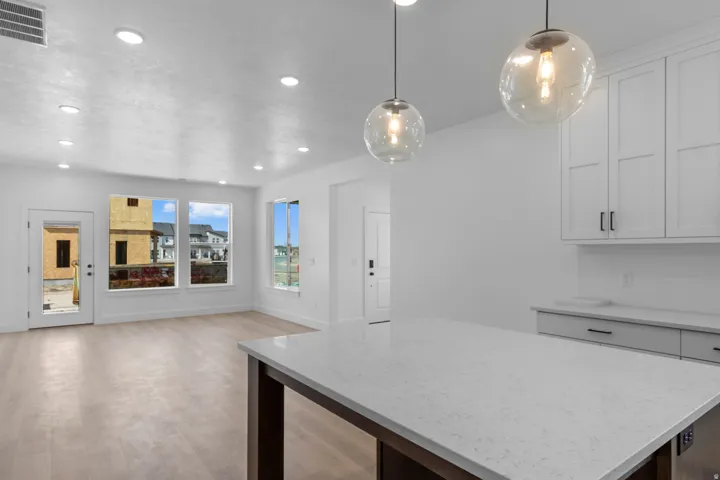 Light wood-finish flooring, recessed ceiling lighting, ample natural light from multiple windows, white shaker cabinetry, and a substantial countertop island