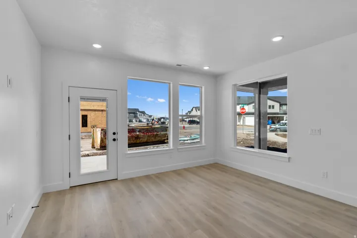 Recessed lighting, wood-finish flooring, white trim, multiple windows, and a glass-paneled door