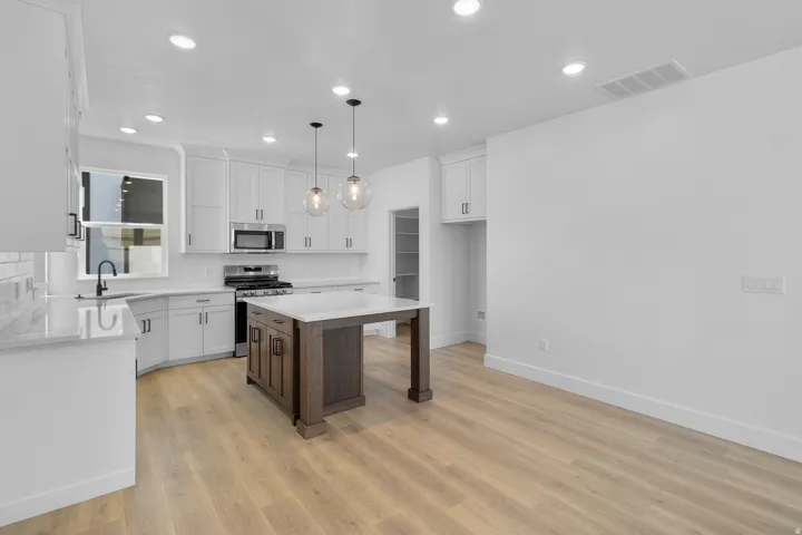 Kitchen featuring white shaker cabinetry, stainless steel appliances, wood-finish flooring, a center island with pendant lighting, and recessed lighting