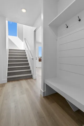 Wood-finish flooring, built-in mudroom bench with shiplap backing, integrated coat hooks, recessed ceiling lighting, and a carpeted staircase