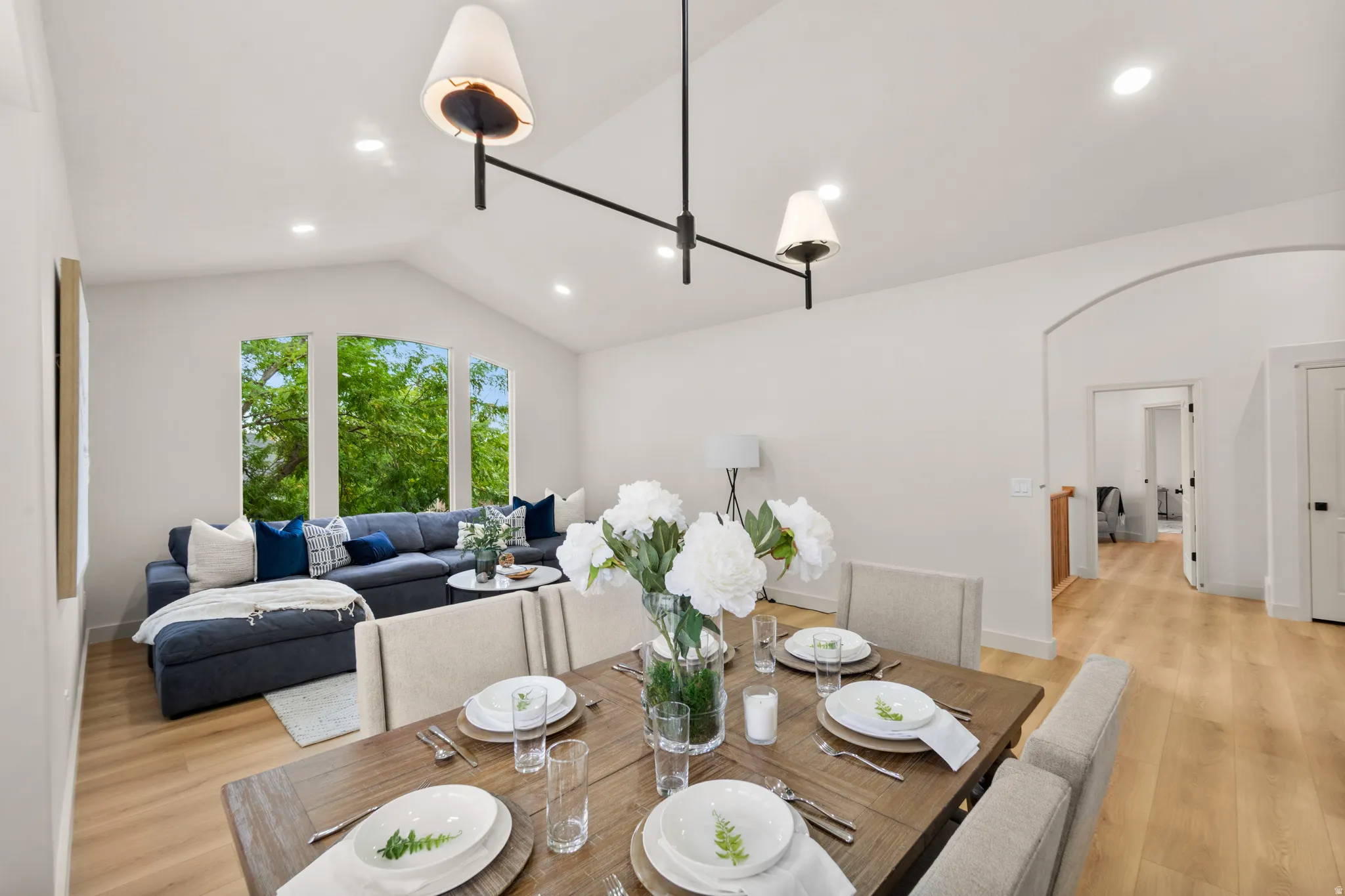 Vaulted ceiling, recessed lighting, wood-finish flooring, arched doorway, and large windows