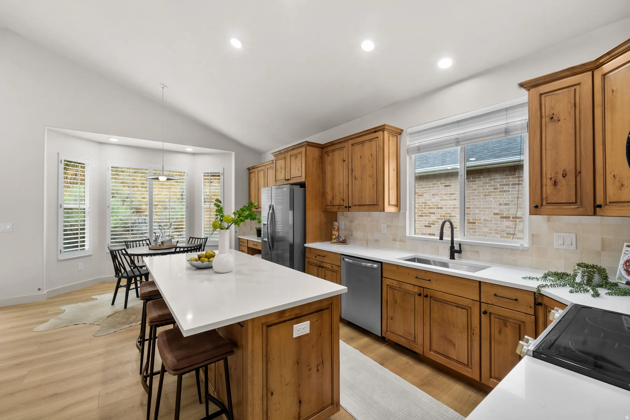 Kitchen featuring a center island with countertop seating, light wood-finish cabinetry, stainless steel appliances, and a vaulted ceiling