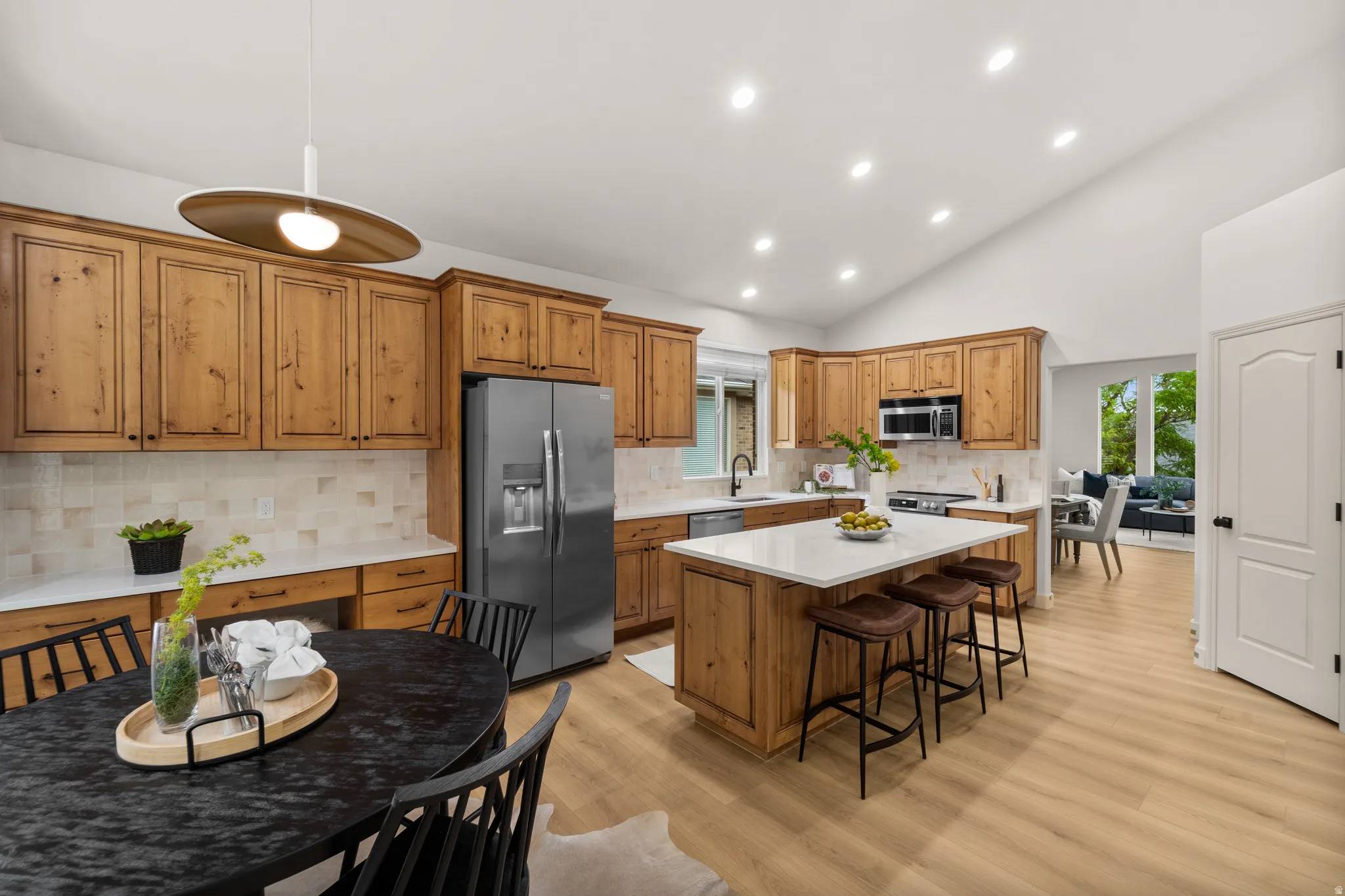 Vaulted ceiling kitchen featuring wood-finish cabinetry, stainless steel appliances, stone countertops, and wood-finish flooring