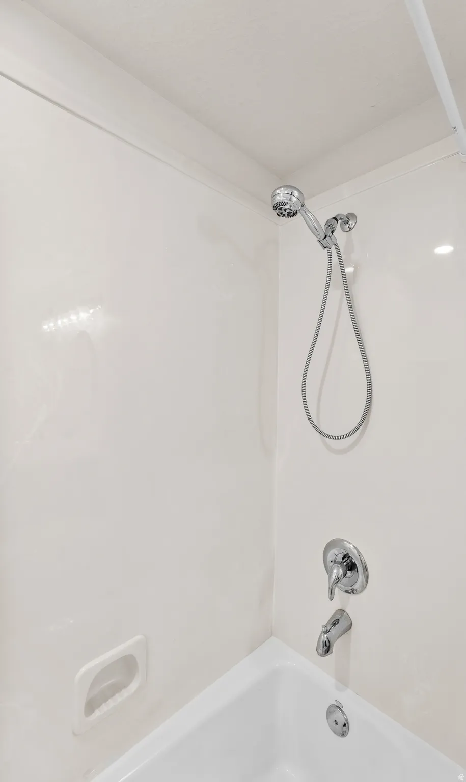 White bathtub with integrated shower, chrome-finish fixtures, and a white soap dish