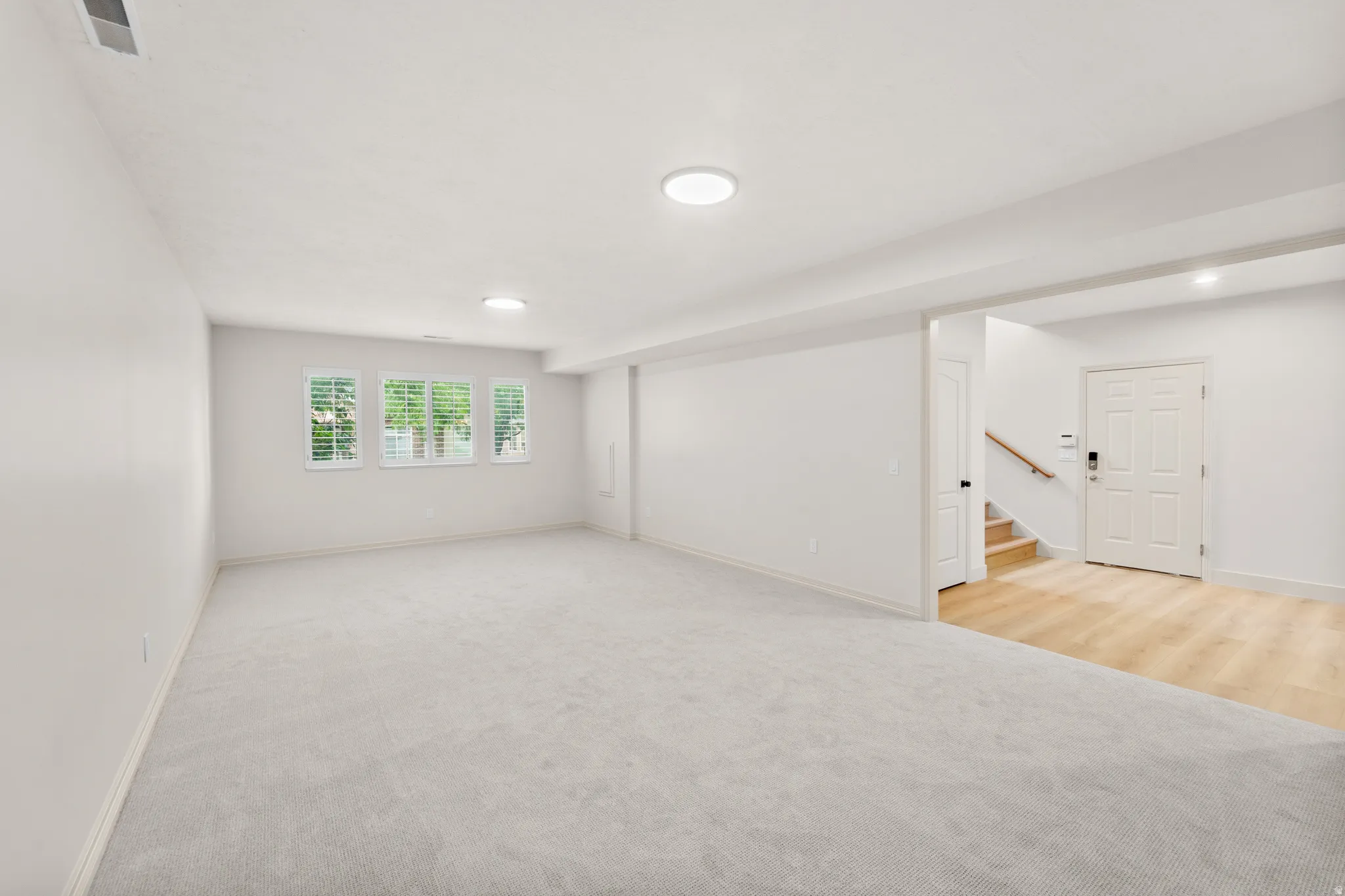 Spacious room with light-colored carpeting, multiple windows featuring plantation shutters, and recessed lighting