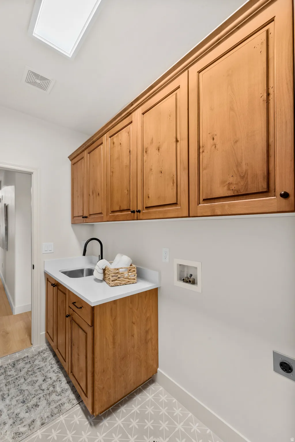 Warm-toned wood cabinetry, built-in sink with a black faucet, white countertop, and patterned floor tile