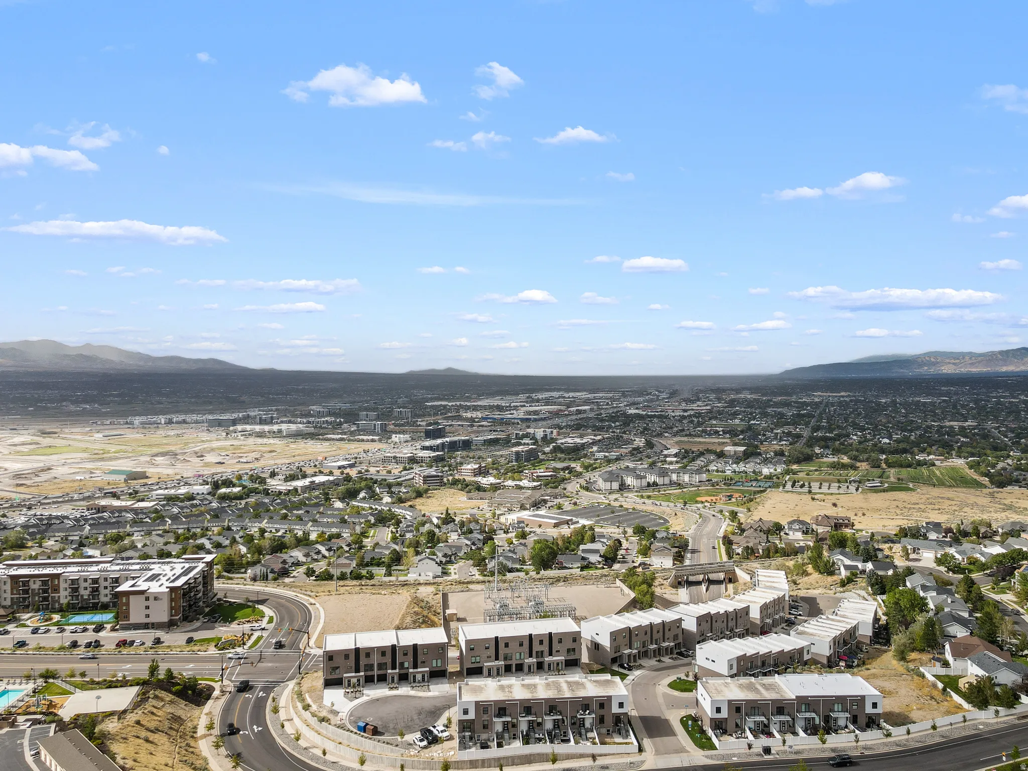 Expansive suburban landscape featuring modern townhomes, developed residential areas, and distant mountainous terrain under a clear sky
