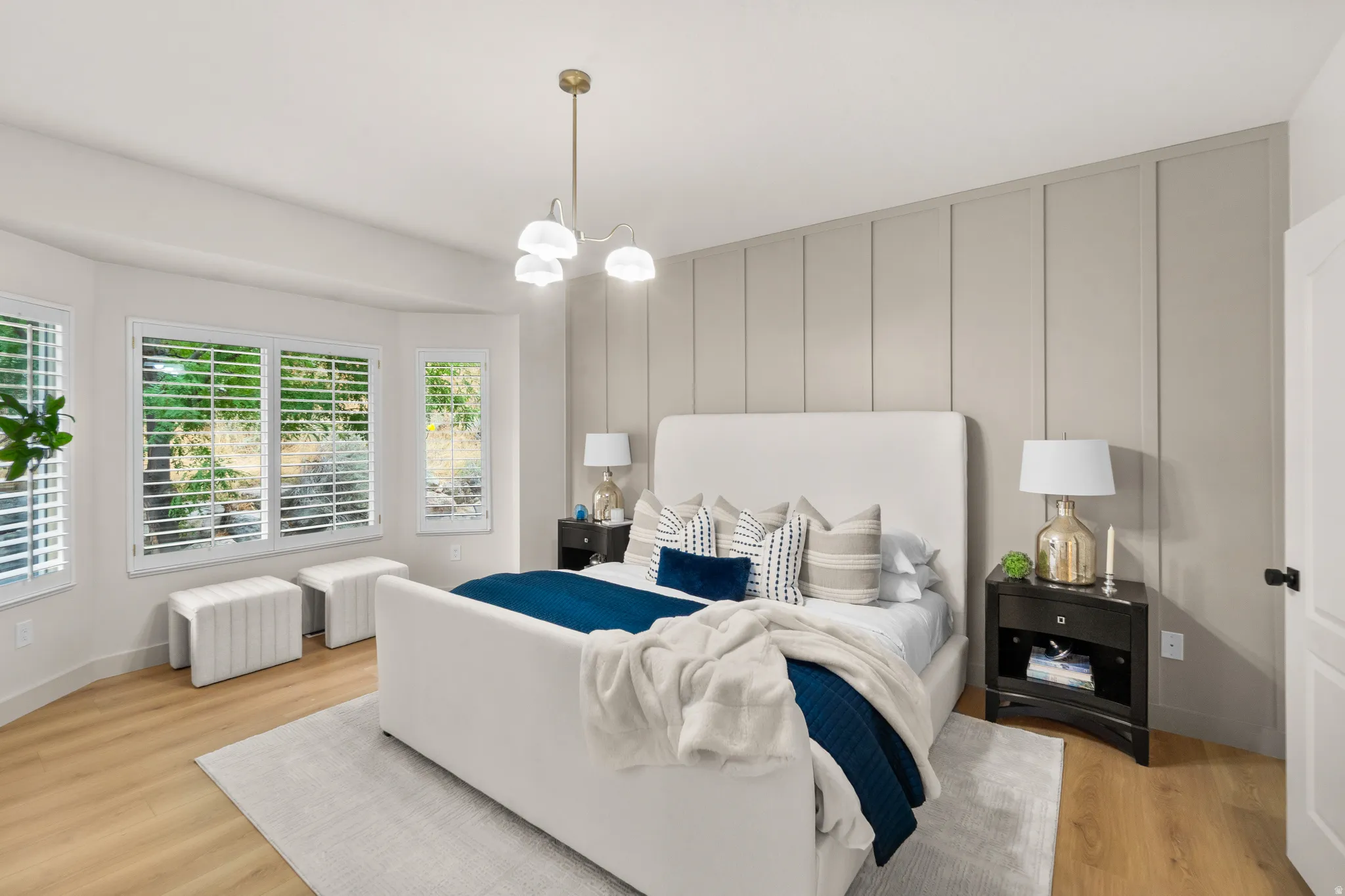 Light wood-finish flooring, accent wall with vertical paneling, contemporary chandelier, multiple windows with plantation shutters, and a white paneled door