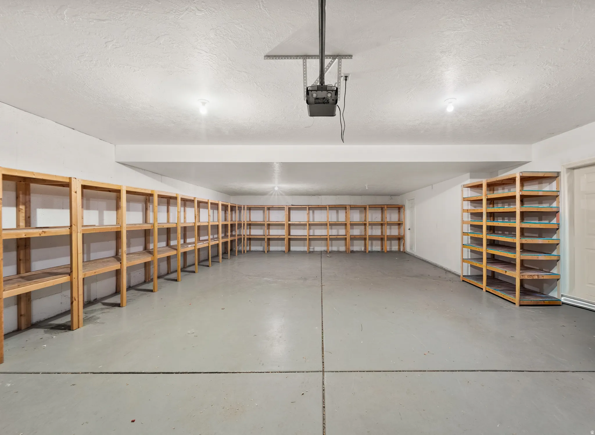 Spacious garage featuring extensive built-in wooden shelving, concrete flooring, and overhead lighting