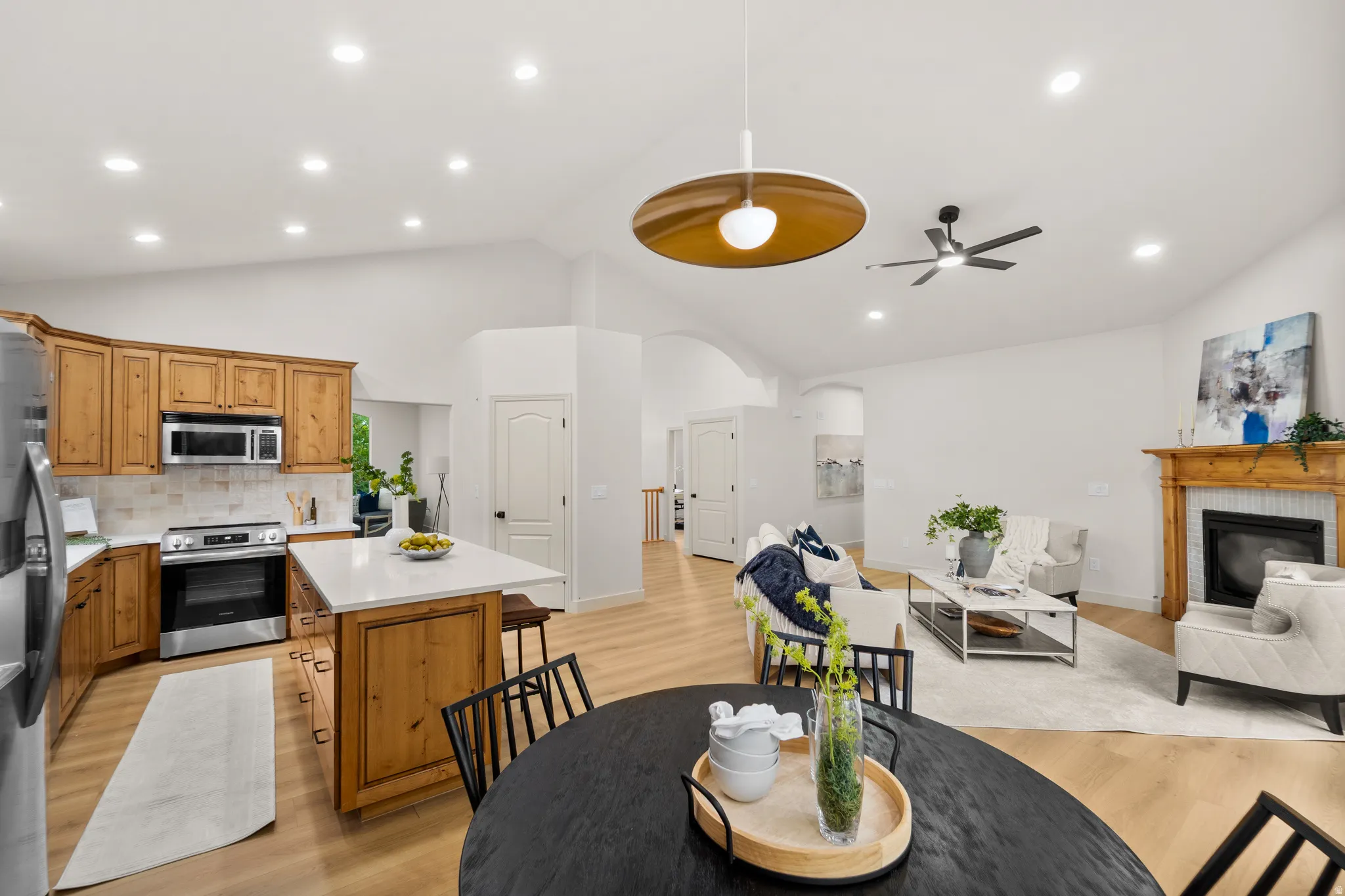 Vaulted ceilings, recessed lighting, wood-finish flooring, a kitchen island with stone countertops, and a fireplace with a wood mantle