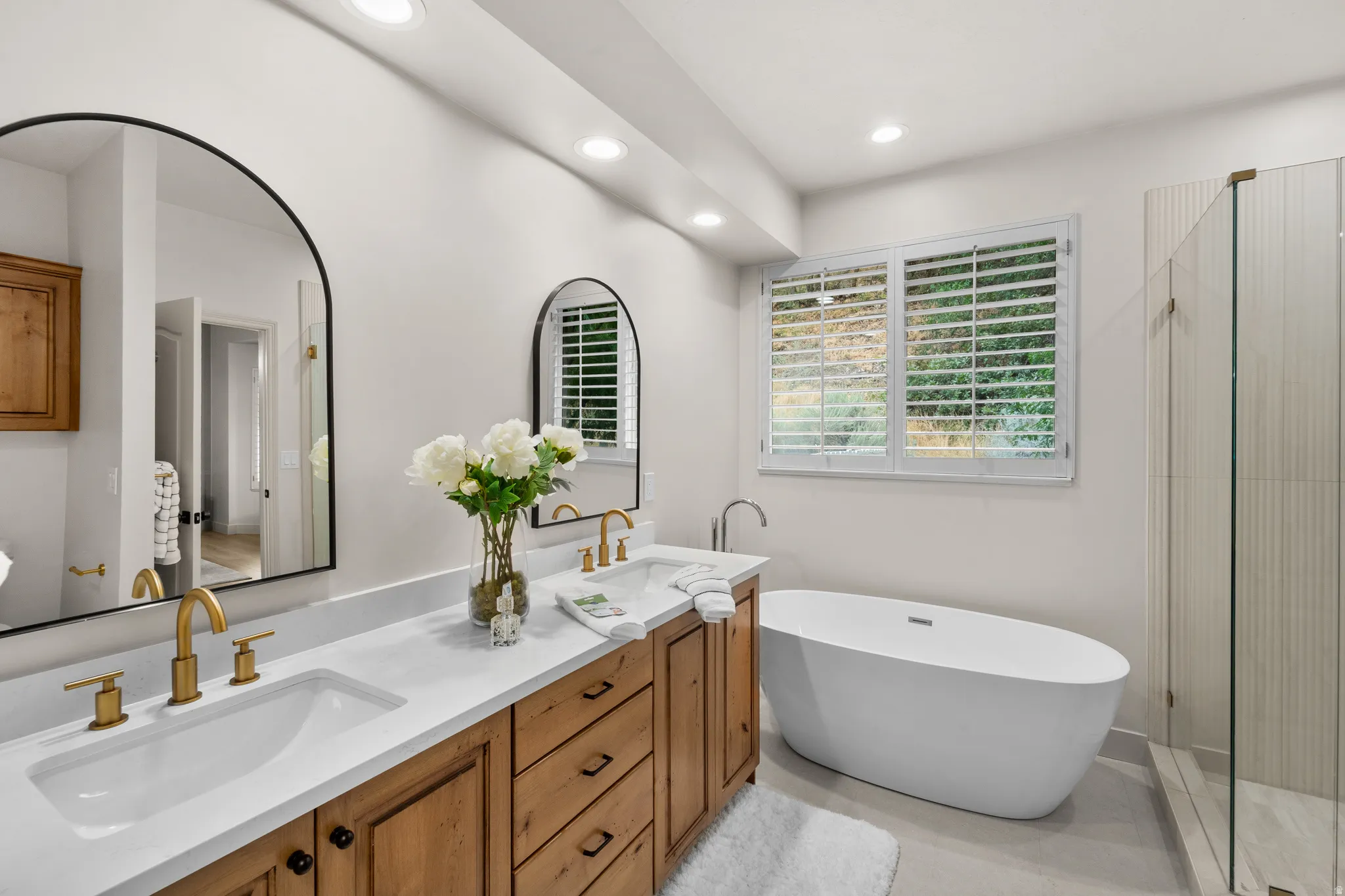 Double vanity with wood-finish cabinetry, white countertops, and gold-tone fixtures