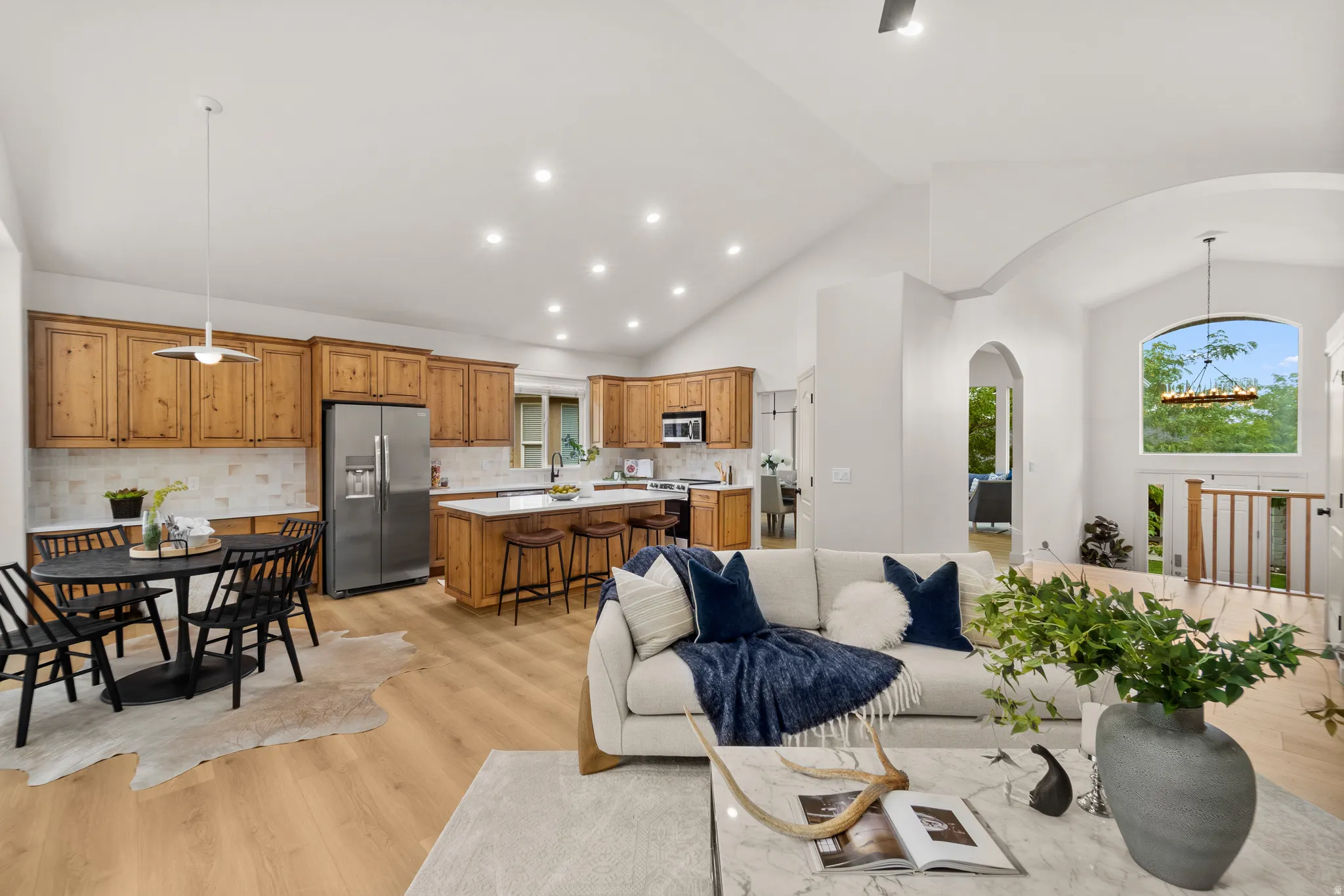 Open concept living space featuring vaulted ceilings, wood-finish flooring, recessed lighting, and a kitchen with wood cabinetry and stainless steel appliances