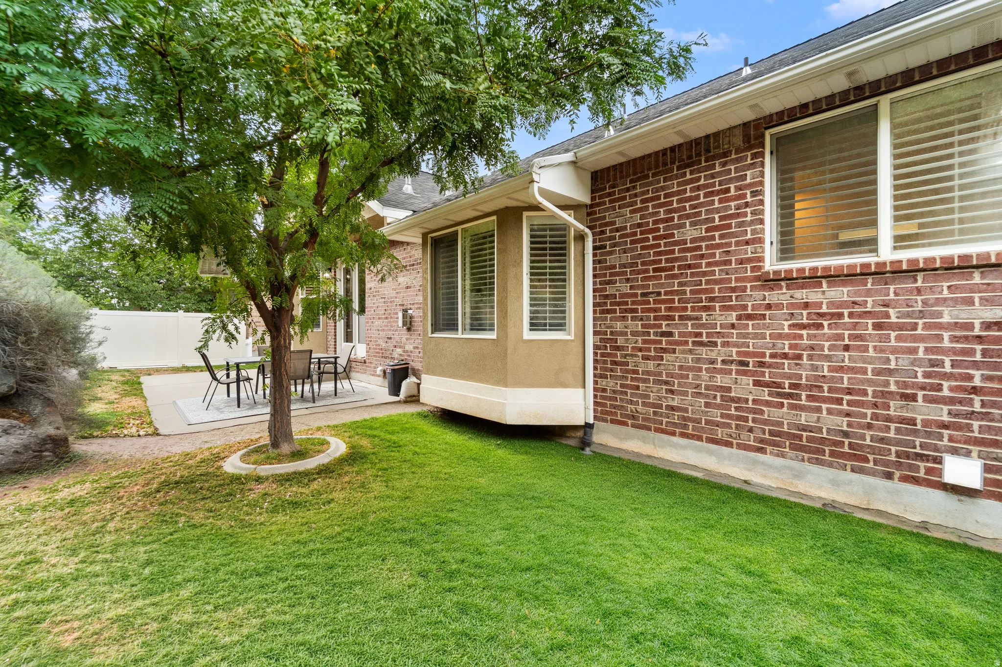 Manicured lawn with mature tree, concrete patio, brick exterior, and bay window