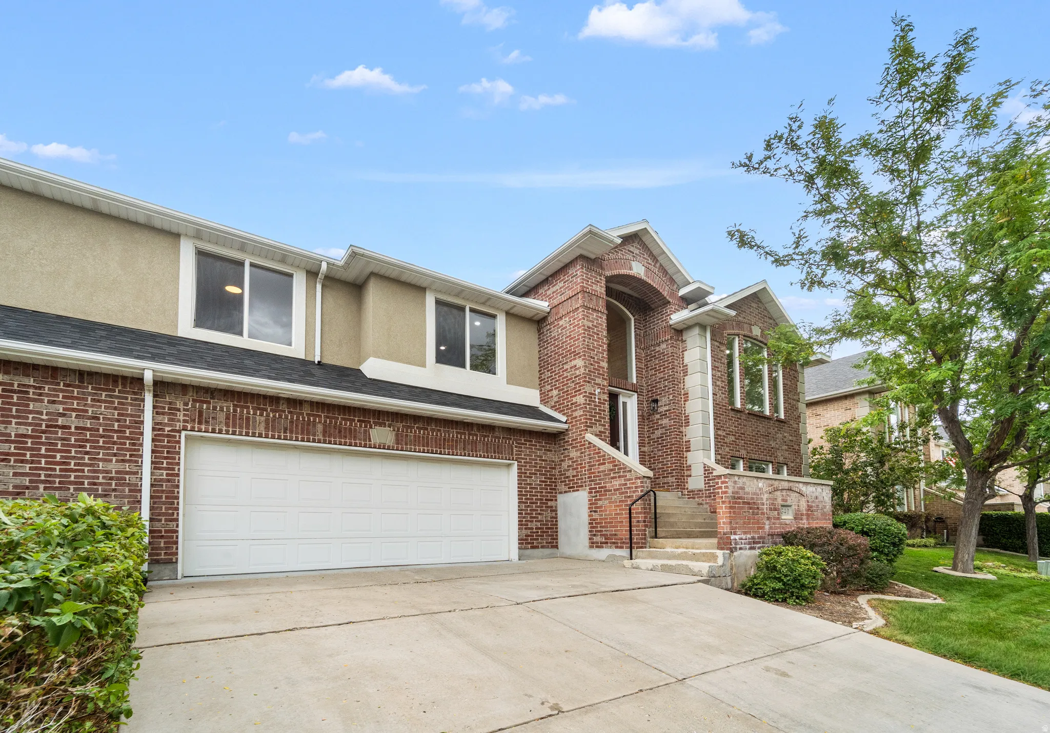 Brick facade with a two-car garage, concrete driveway, and established landscaping