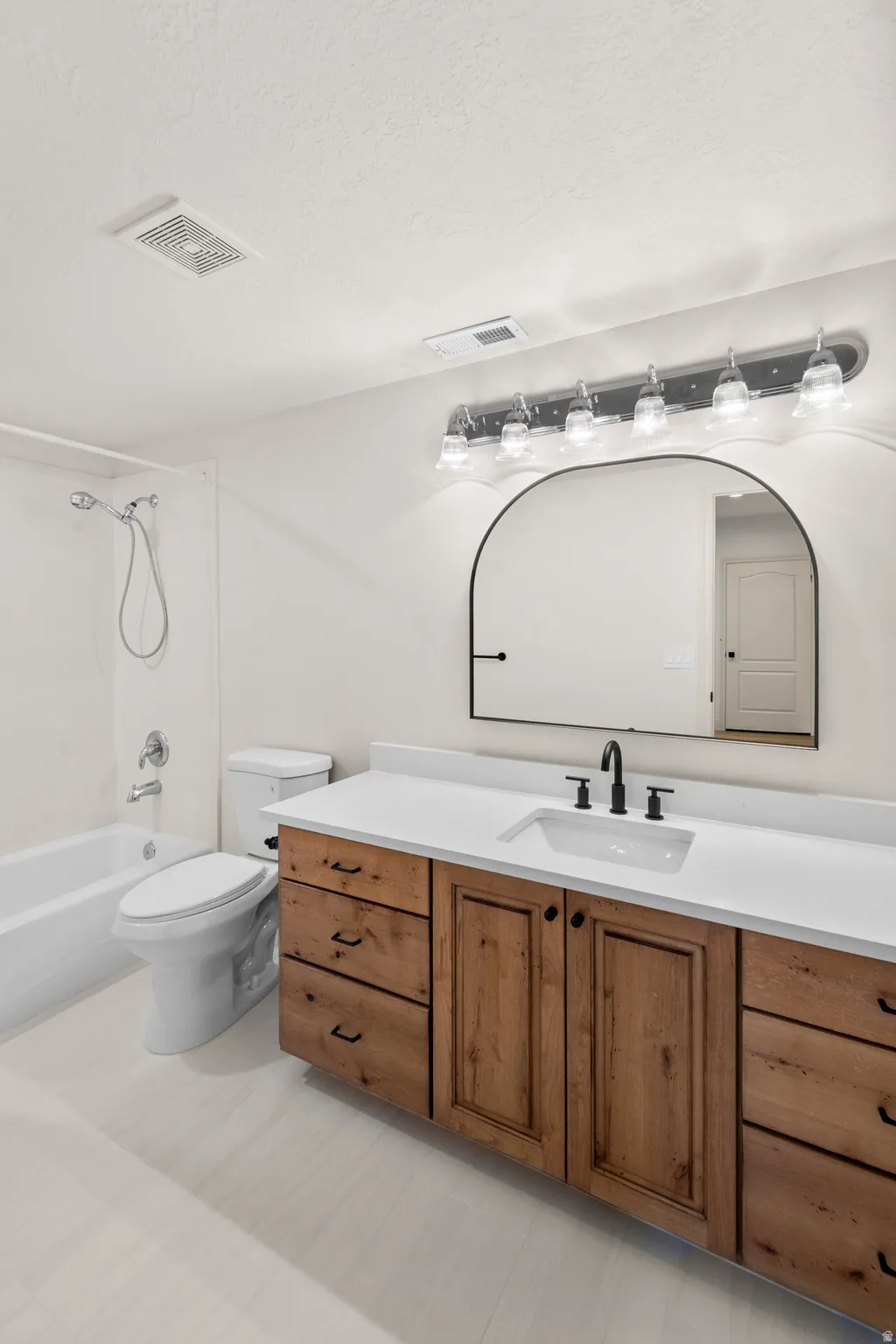 Floating wood-finish vanity with a white countertop and undermount sink, complemented by a black-framed arched mirror and black-finish faucet