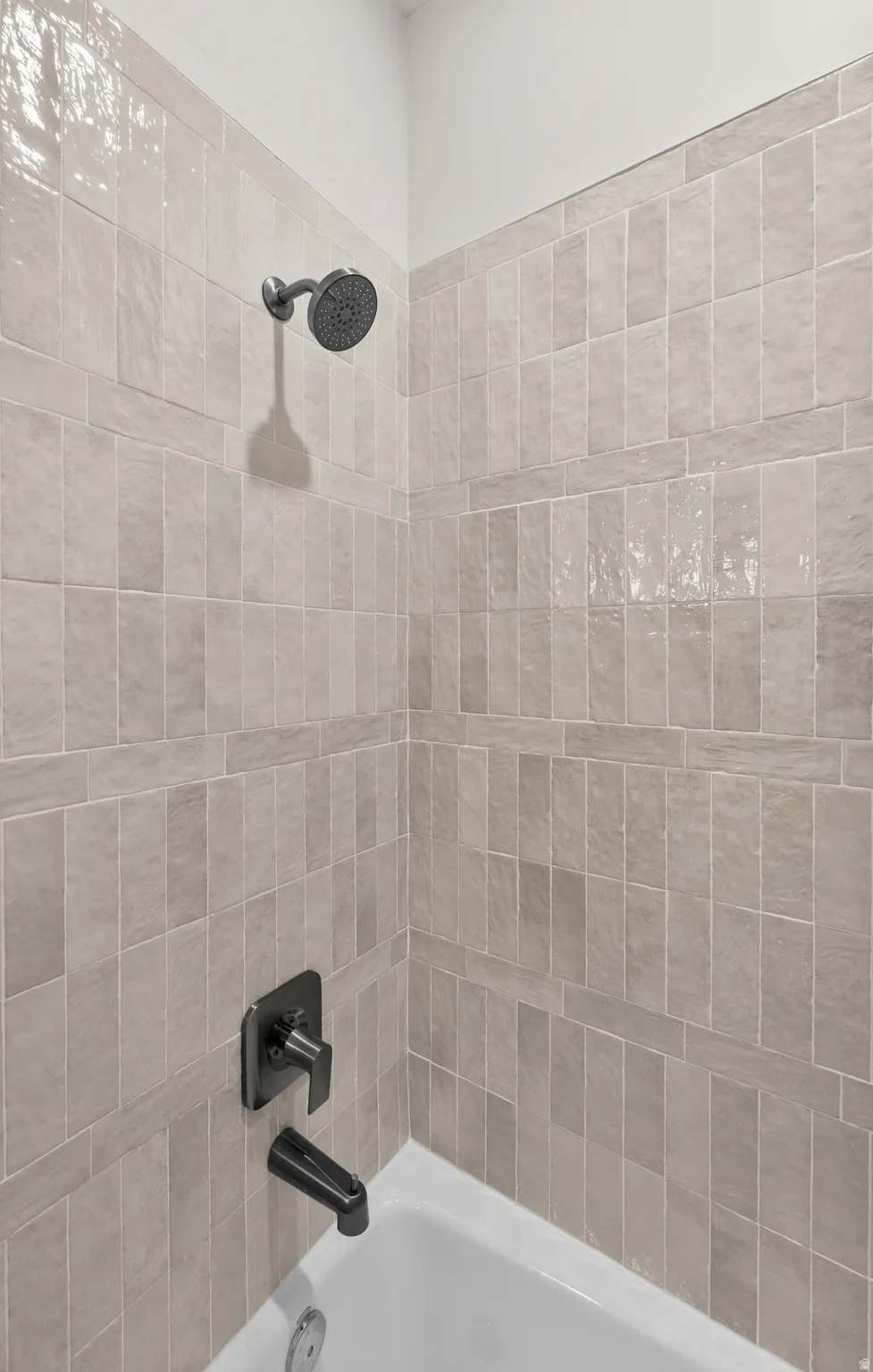 Bathtub with a matte black faucet and shower head, surrounded by light-toned rectangular tile walls