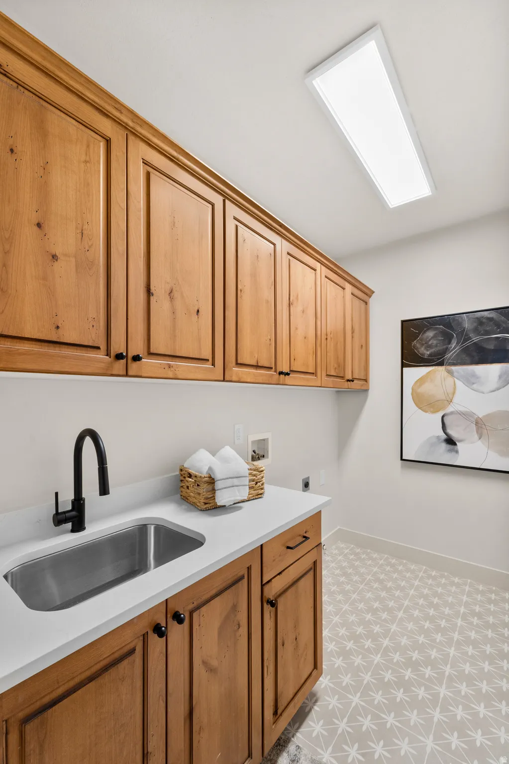 Wood-finish cabinetry, stainless steel sink, solid surface countertop, matte black faucet, and patterned floor tile