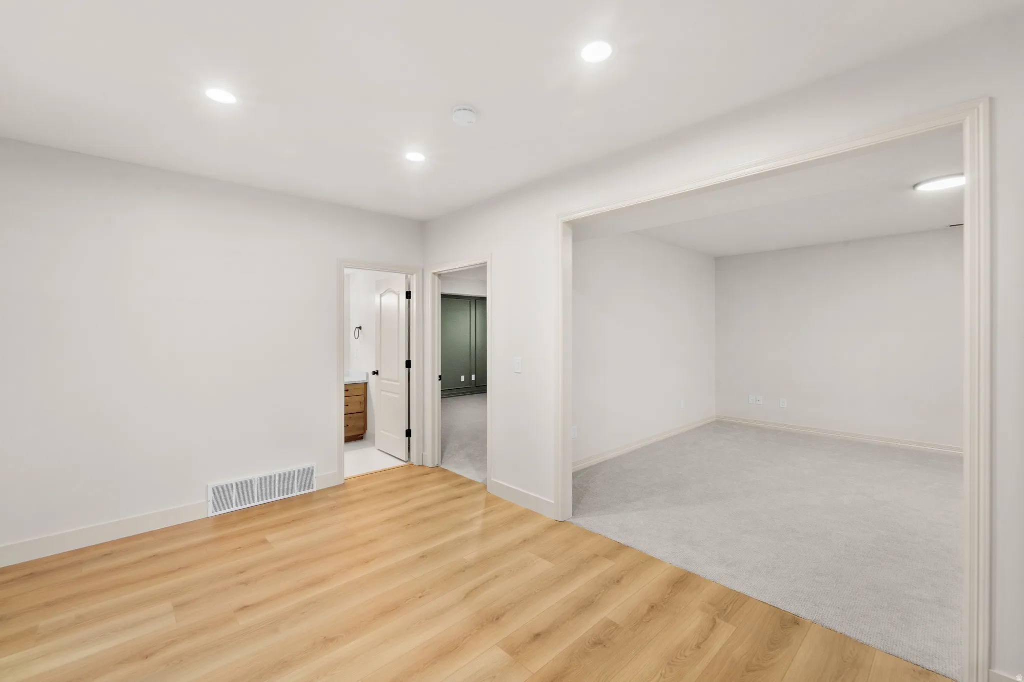 Recessed lighting, wood-finish flooring, white trim, and a doorway to a separate room with carpet