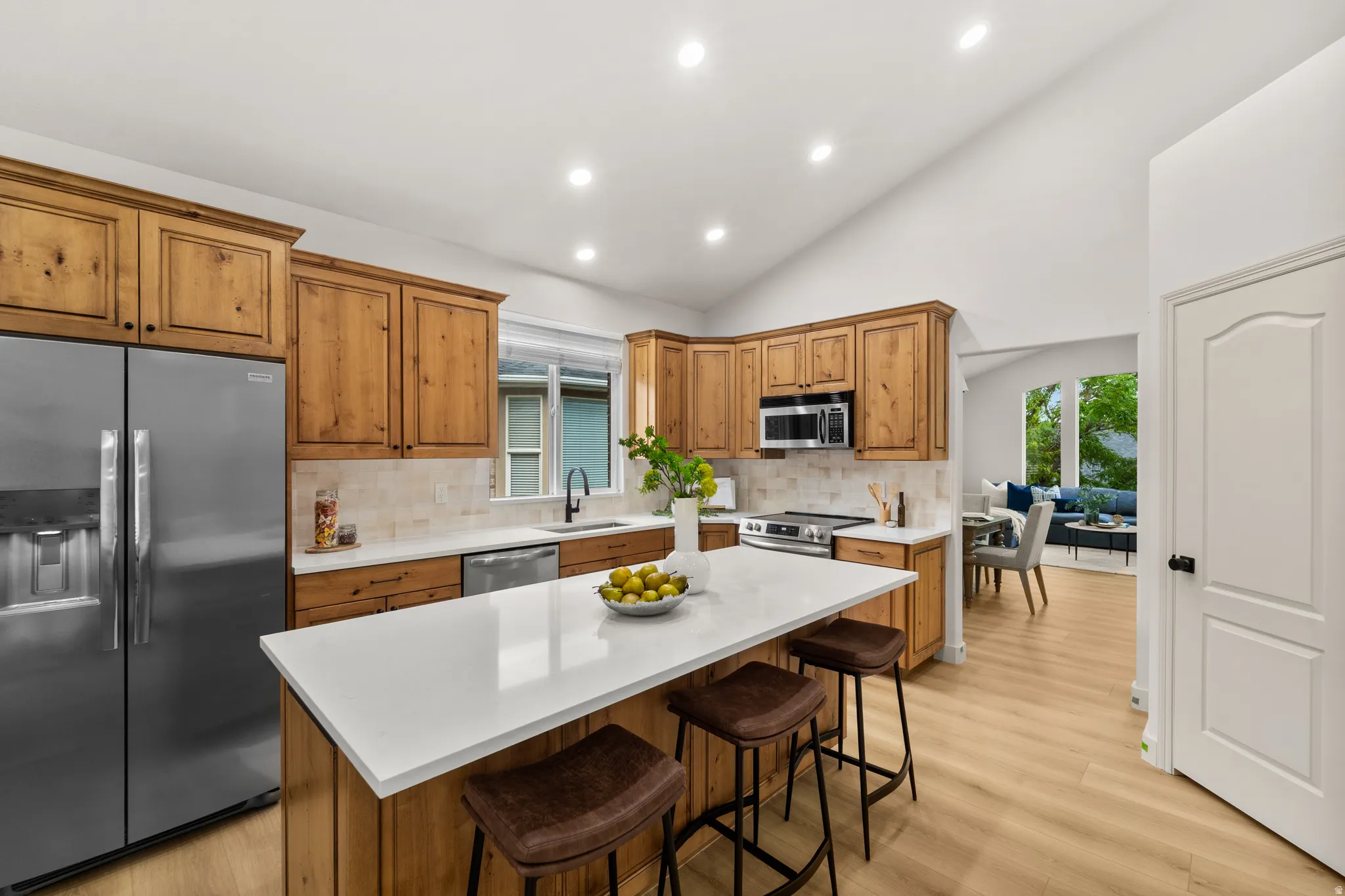 Kitchen featuring wood-finish cabinetry, stainless steel appliances, a center island with counter seating, and light-tone wood-finish flooring